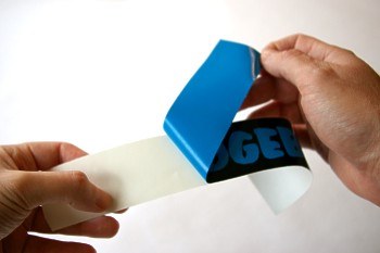 Hands peeling the backing from a glossy vinyl bumper sticker